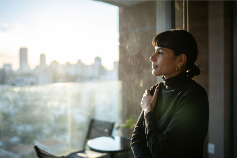 A woman looking out of the window at the city, thinking about her epilepsy self-management techniques.