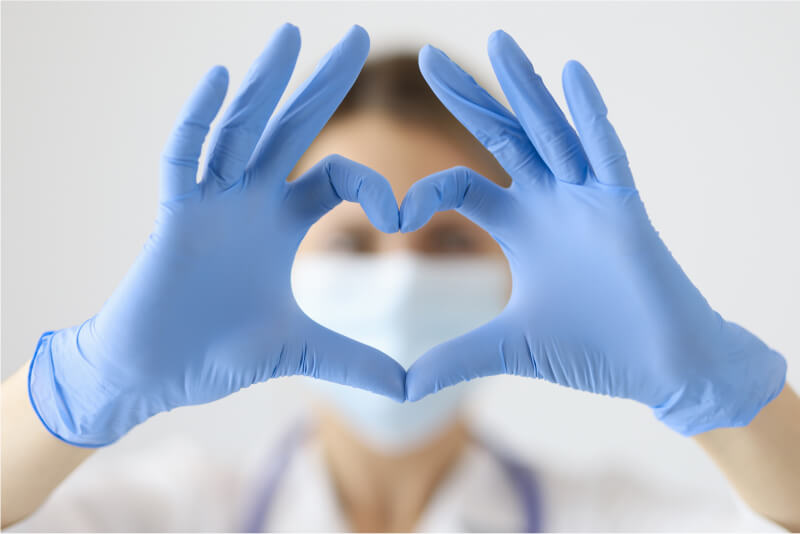 Doctor with gloves holding her hands to make a heart shape, creating a link to cardiovascular disease.