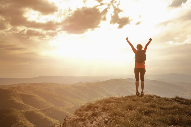 Woman standing on top of a mountain, feeling on top of the world because her atopic dermatitis is under control.
